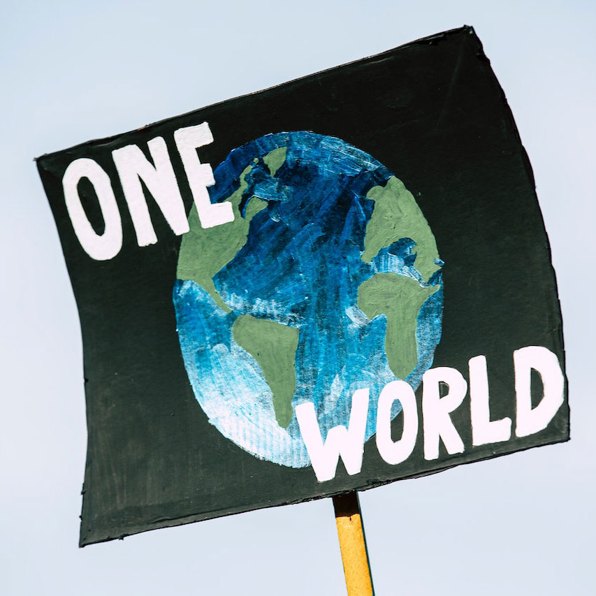 Placard with a drawing of the world on a black background with 'ONE WORLD' written across in white capitals