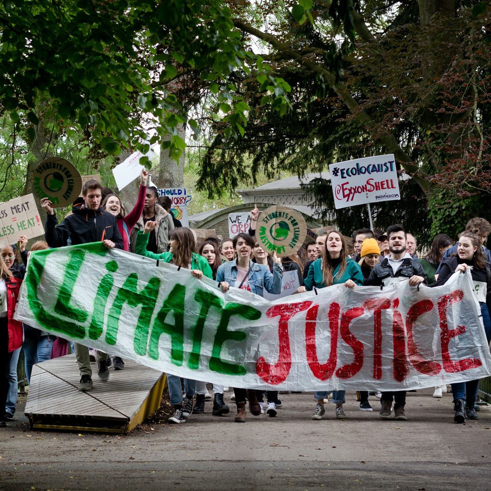 Photo of young people walking down the street holding a large white banner with the wording 'CLIMATE JUSTICE' and a number of smaller placards